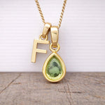 Close-up of personalised gold-plated F initial charm and light green pear-shaped peridot pendant on a fine chain, August birthstone necklace