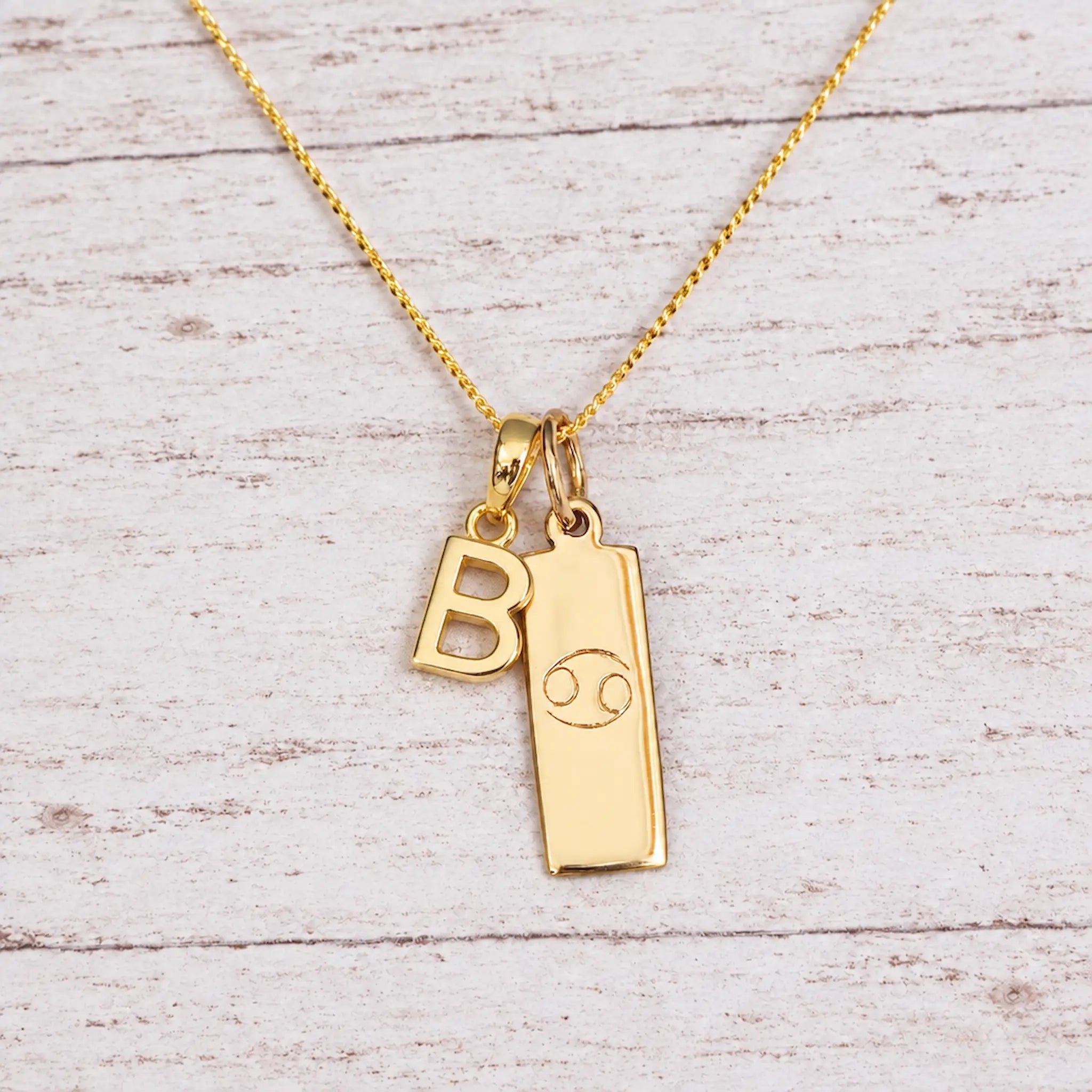 Gold Initial and Cancer Zodiac Necklace with letter B pendant on light wood