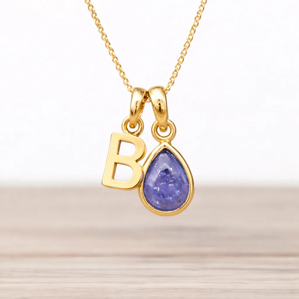 Gold necklace with 'B' pendant and natural tanzanite teardrop-shaped gemstone on a light background