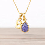 Gold necklace with 'B' pendant and natural tanzanite teardrop-shaped gemstone on a light background
