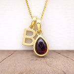 gold b initial and january birthstone garnet necklace hanging above a wooden surface
