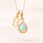 Gold necklace with 'B' pendant and teardrop-shaped opal stone on a light background
