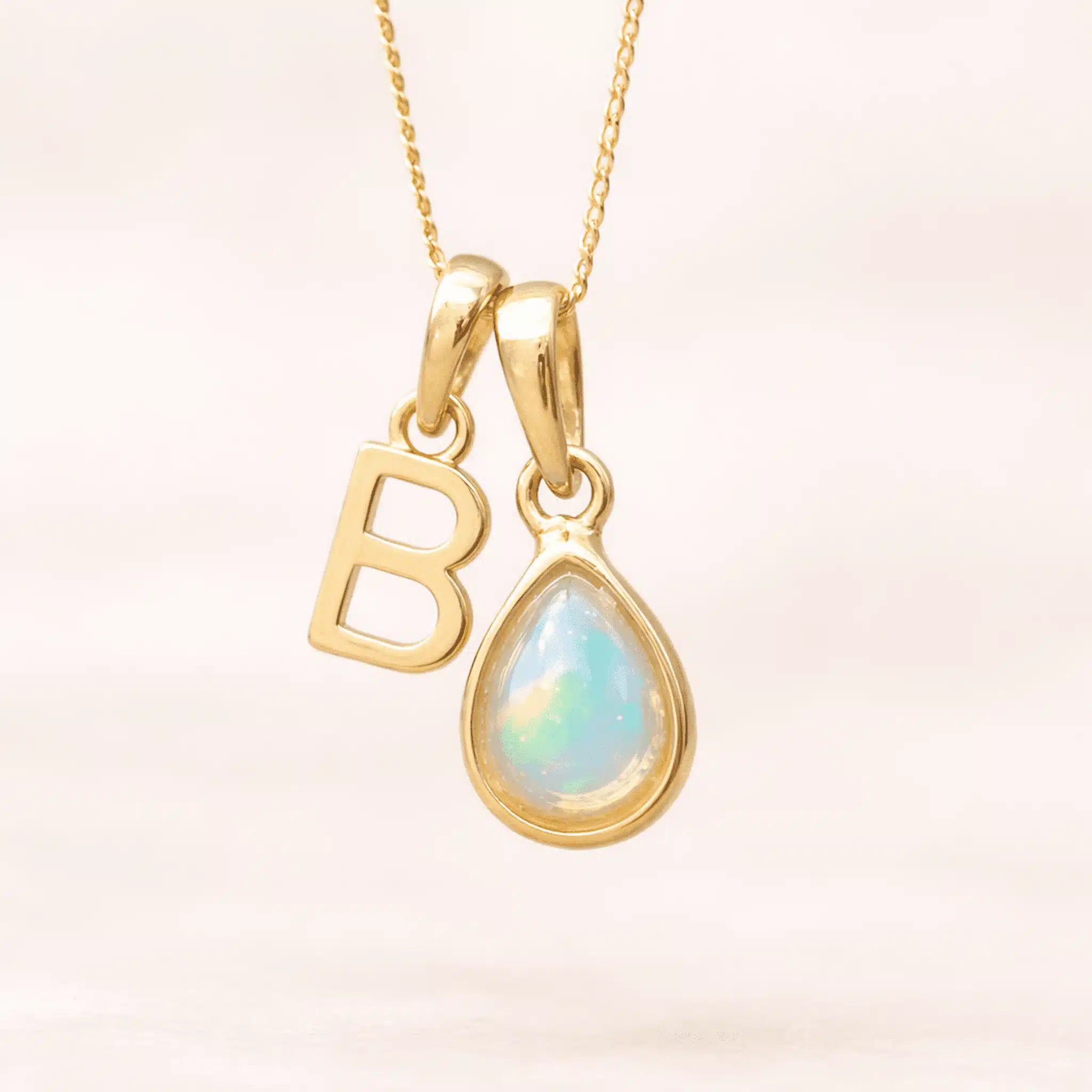 Gold October birthstone necklace with a pear-shaped natural opal pendant and letter 'B' charm with a light background.