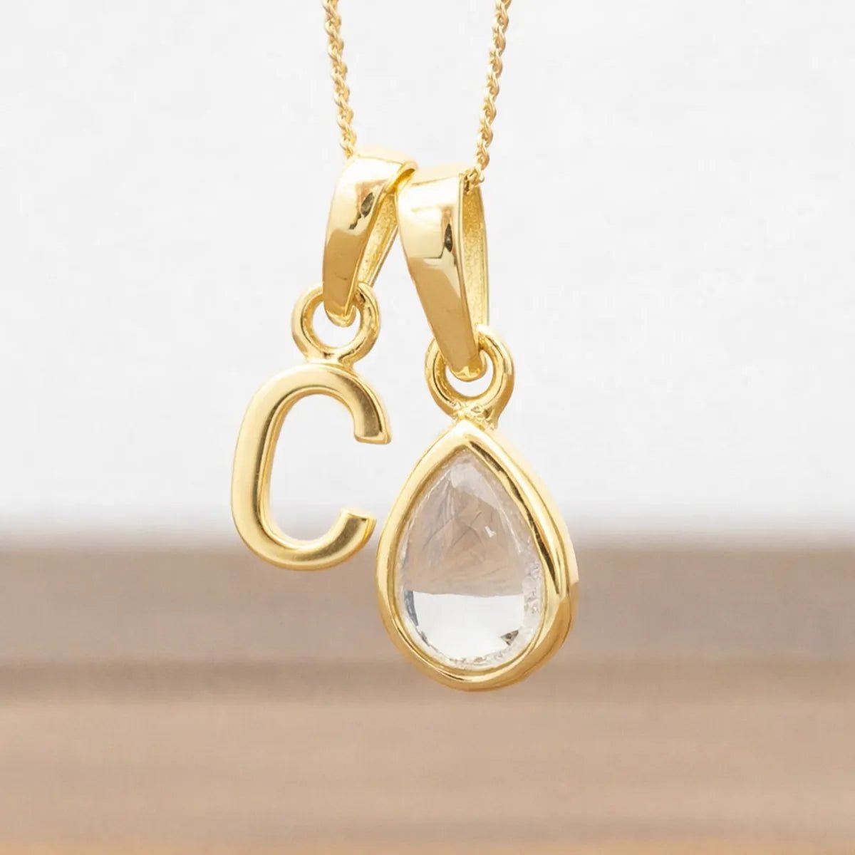 Gold necklace with 'C' pendant and teardrop-shaped herkimer quartz clear stone on a light background