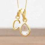 Gold necklace with 'C' pendant and teardrop-shaped herkimer quartz clear stone on a light background