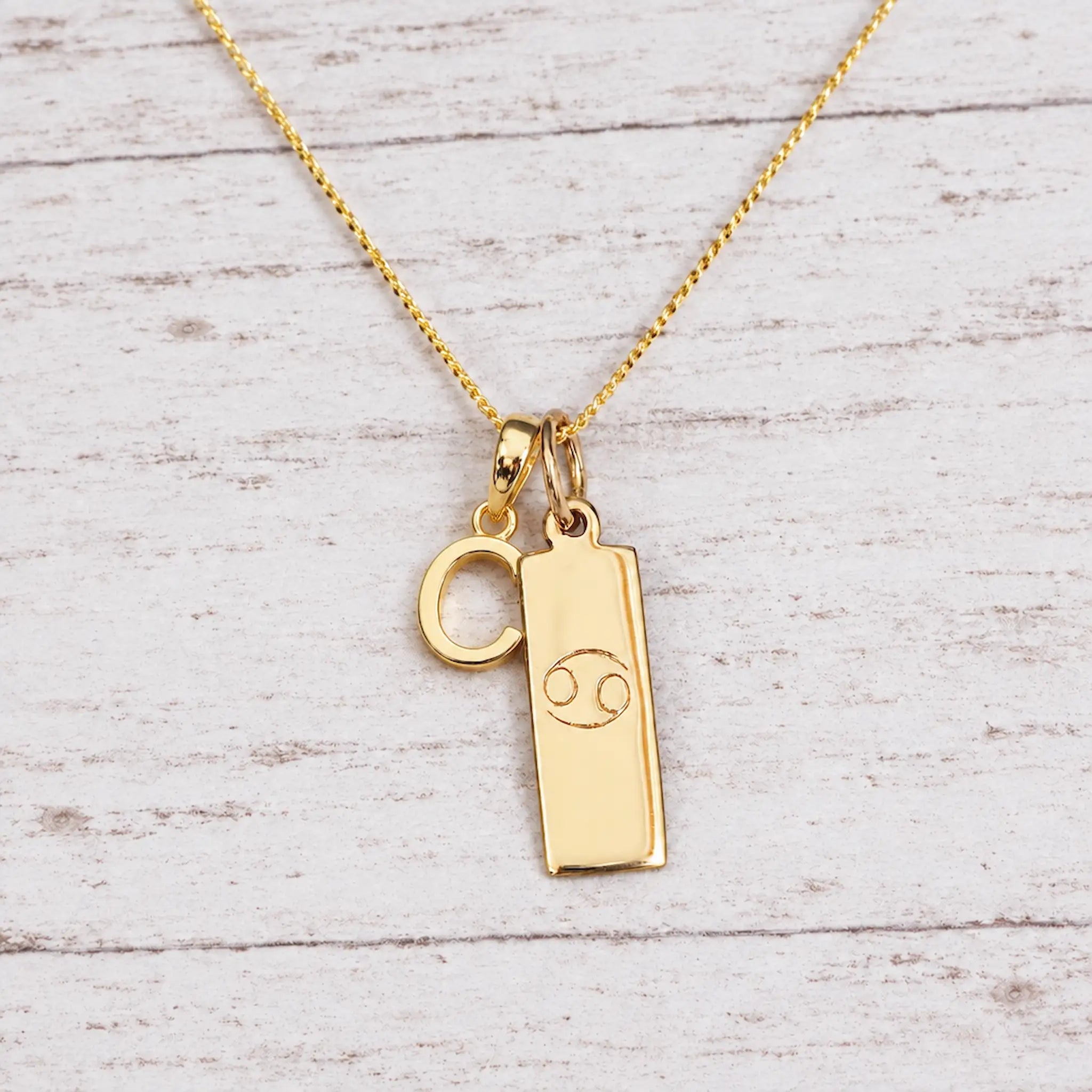 Gold Initial and Cancer Zodiac Necklace with letter C pendant on light wood
