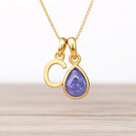 Gold necklace with a 'C' pendant and purple and blue teardrop tanzanite gemstone on a light background