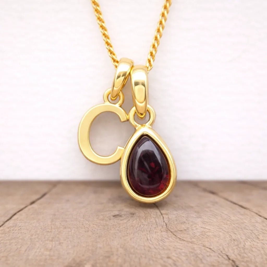 gold c initial and january birthstone garnet necklace hanging above a wooden surface