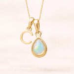 Gold October birthstone necklace with a pear-shaped natural opal pendant and letter 'C' charm with a light background.