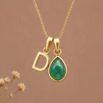 Gold Initial D and May Birthstone Emerald Necklace against a warm background