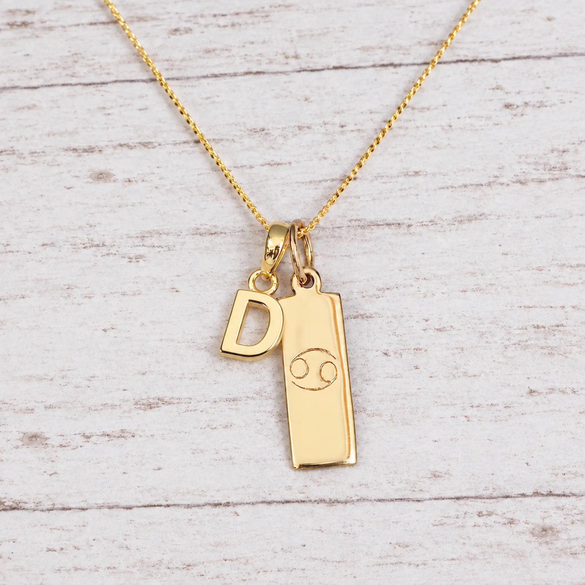 Gold Initial and Cancer Zodiac Necklace with letter D pendant on light wood