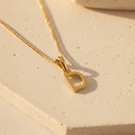Gold necklace with a 'D' pendant on a beige surface