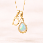 Gold necklace with a teardrop-shaped opal pendant and letter 'D' charm on a light pink background