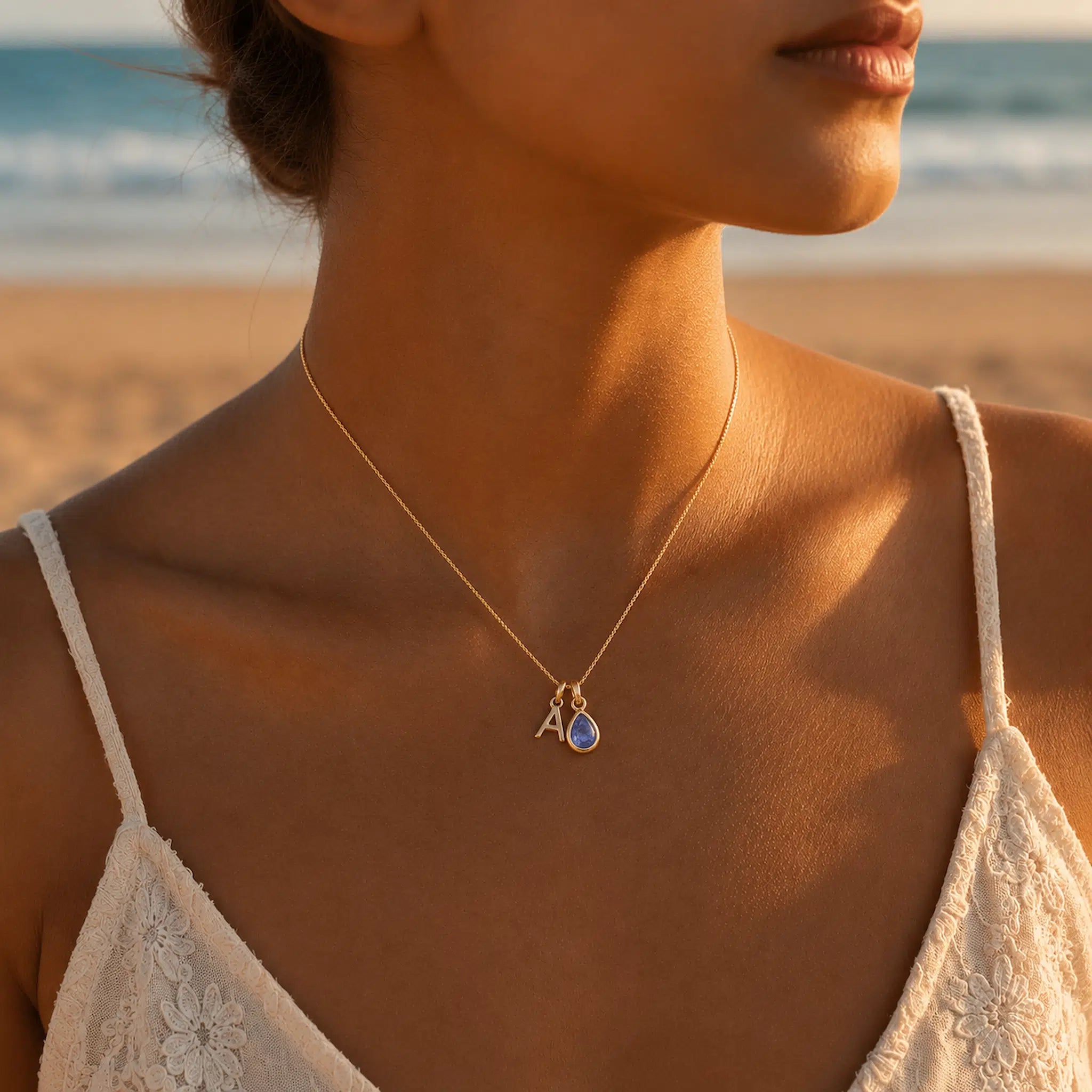 Woman wearing a gold fine chain necklace with a A letter pendant and december birthstone tanzanite pendant on a beach