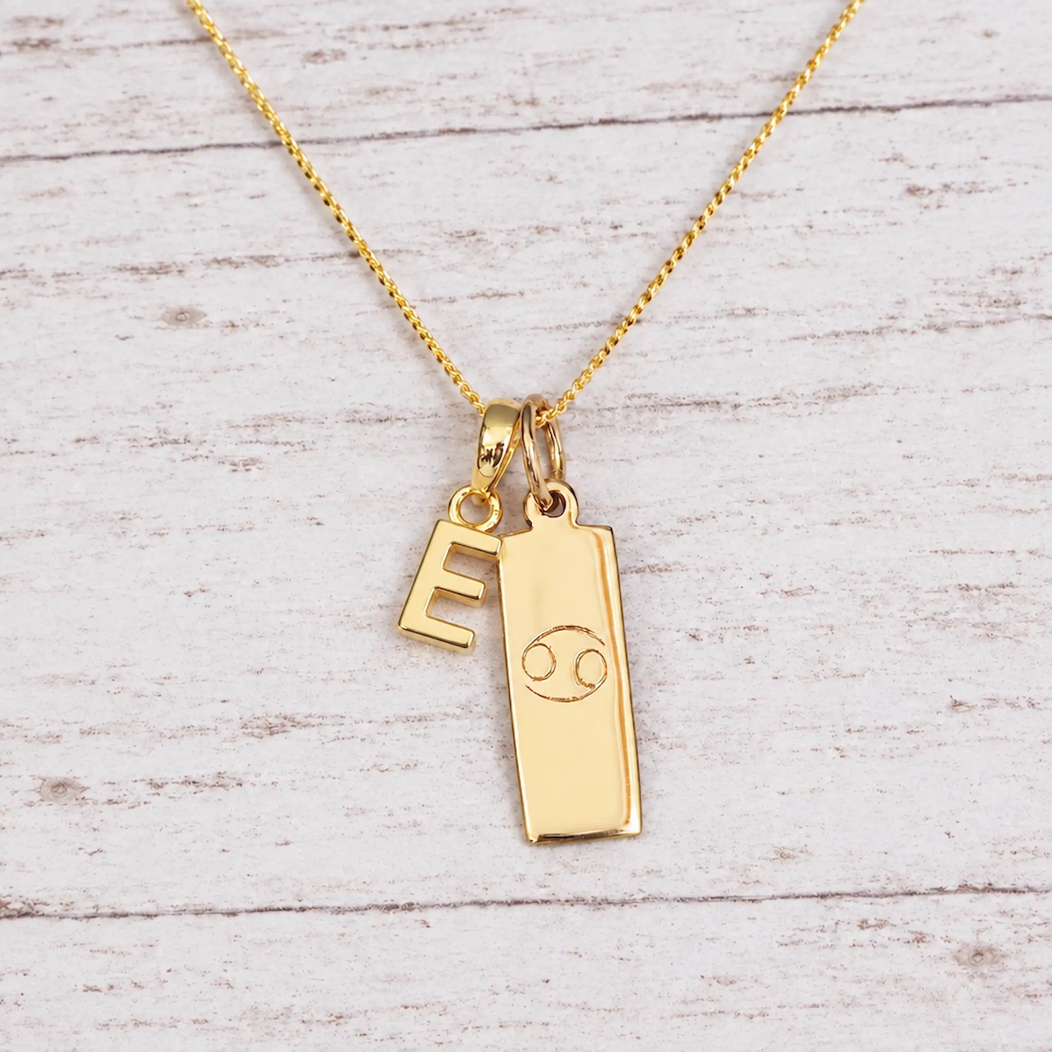 Gold Initial and Cancer Zodiac Necklace with letter E pendant on light wood