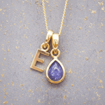 Gold necklace with 'E' pendant and purple teardrop tanzanite pendant on gray background