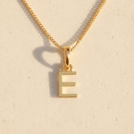 Gold necklace with a 'E' pendant on a beige background
