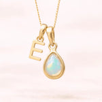 Gold October birthstone necklace with a pear-shaped natural opal pendant and letter 'E' charm with a light background.