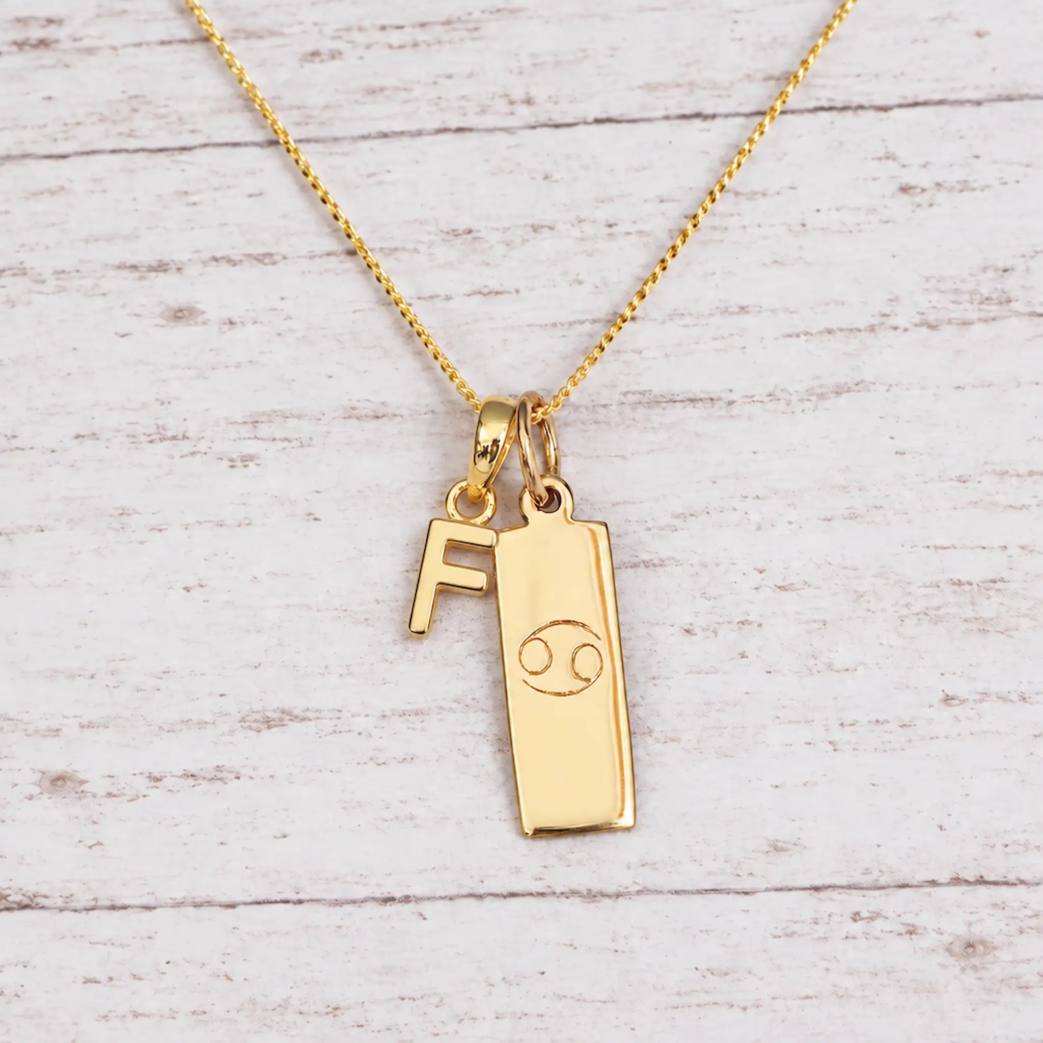 Gold Initial and Cancer Zodiac Necklace with letter F pendant on light wood