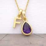 Gold necklace with 'F' pendant and purple amethyst teardrop gem on a light background