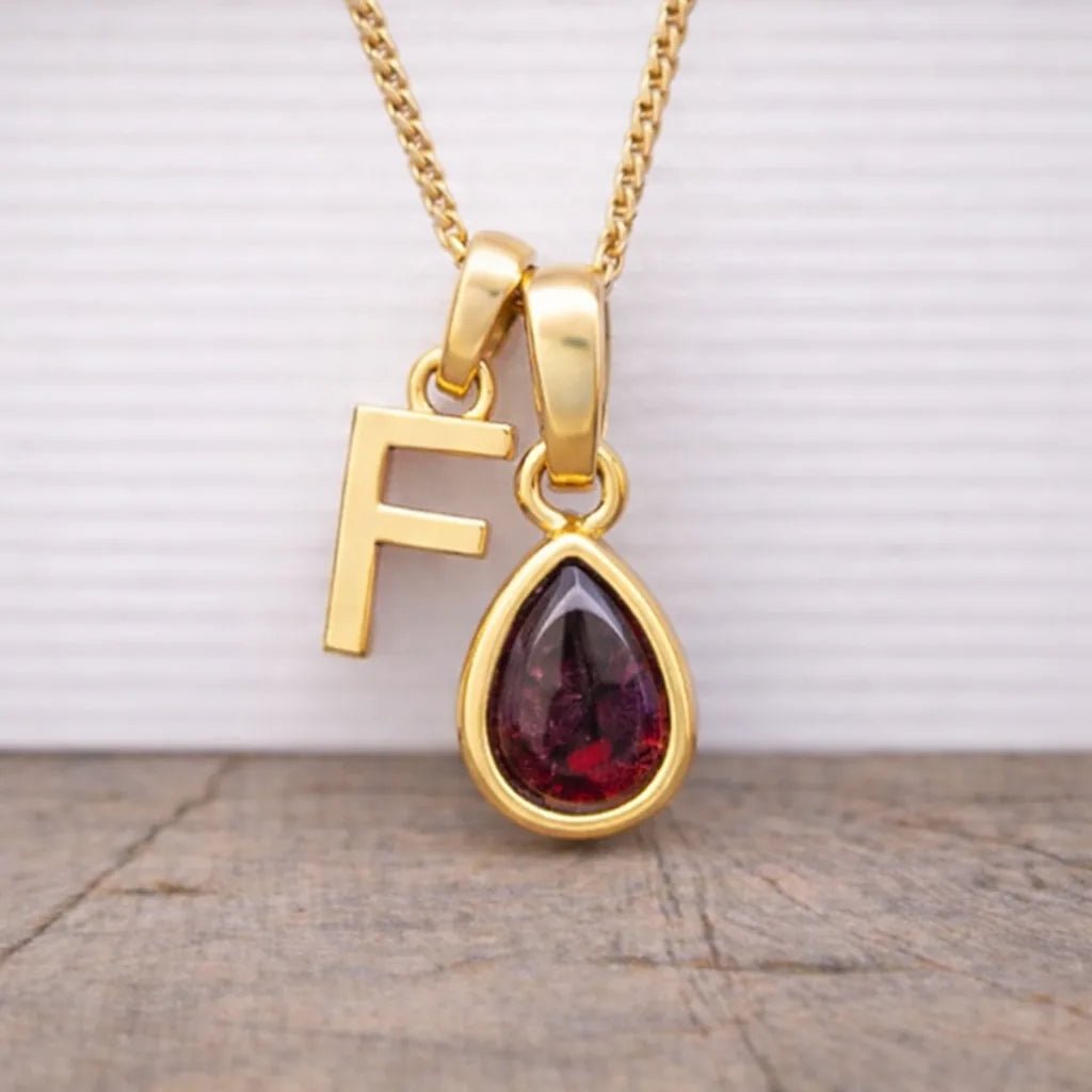 gold f initial and january birthstone garnet necklace hanging above a wooden surface