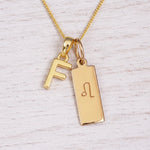 Gold initial and Leo zodiac necklace with a letter F pendant and engraved Leo bar on white wood, close-up