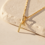 Gold necklace with a 'F' pendant on a beige stone background