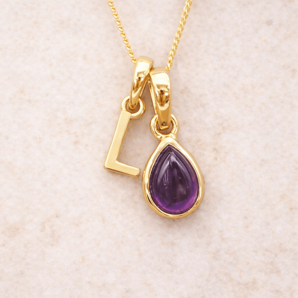 Gold initial L necklace with a purple teardrop amethyst pendant on a beige background