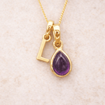 Gold initial L necklace with a purple teardrop amethyst pendant on a beige background