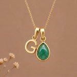Gold Initial G and May Birthstone Emerald Necklace against a warm background