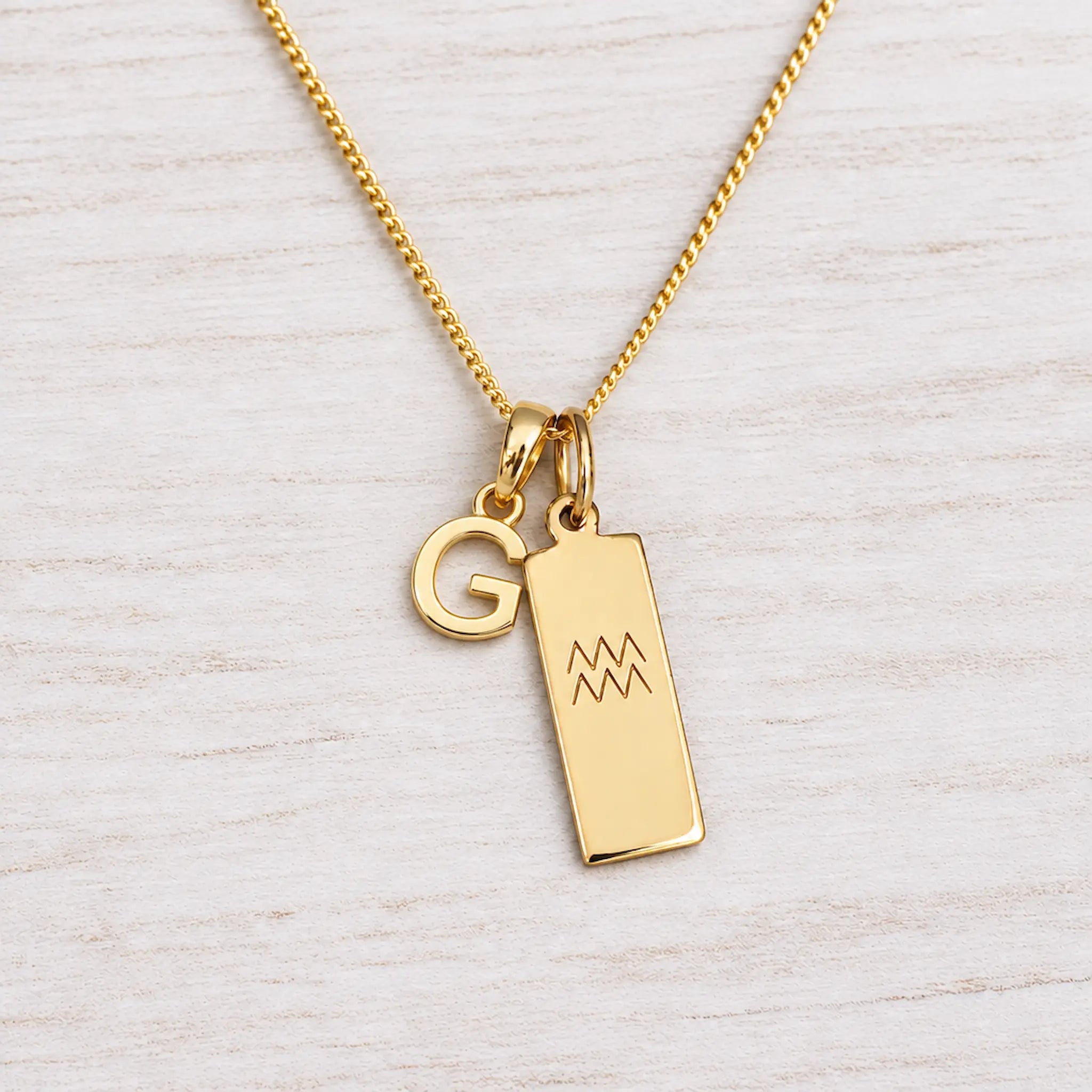 Gold Initial and Aquarius Zodiac Necklace with letter G pendant on light wood
