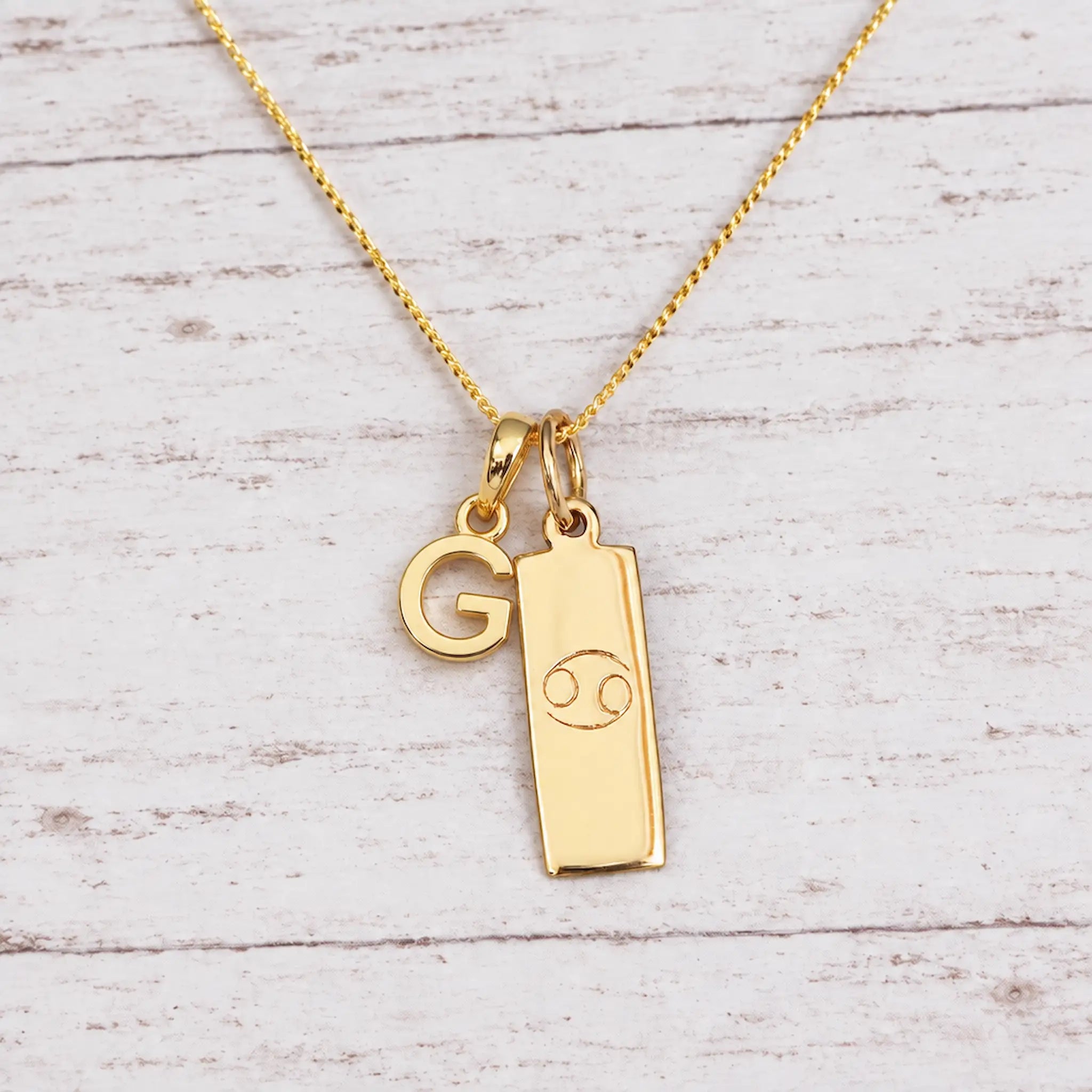 Gold Initial and Cancer Zodiac Necklace with letter G pendant on light wood
