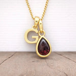 gold g initial and january birthstone garnet necklace hanging above a wooden surface