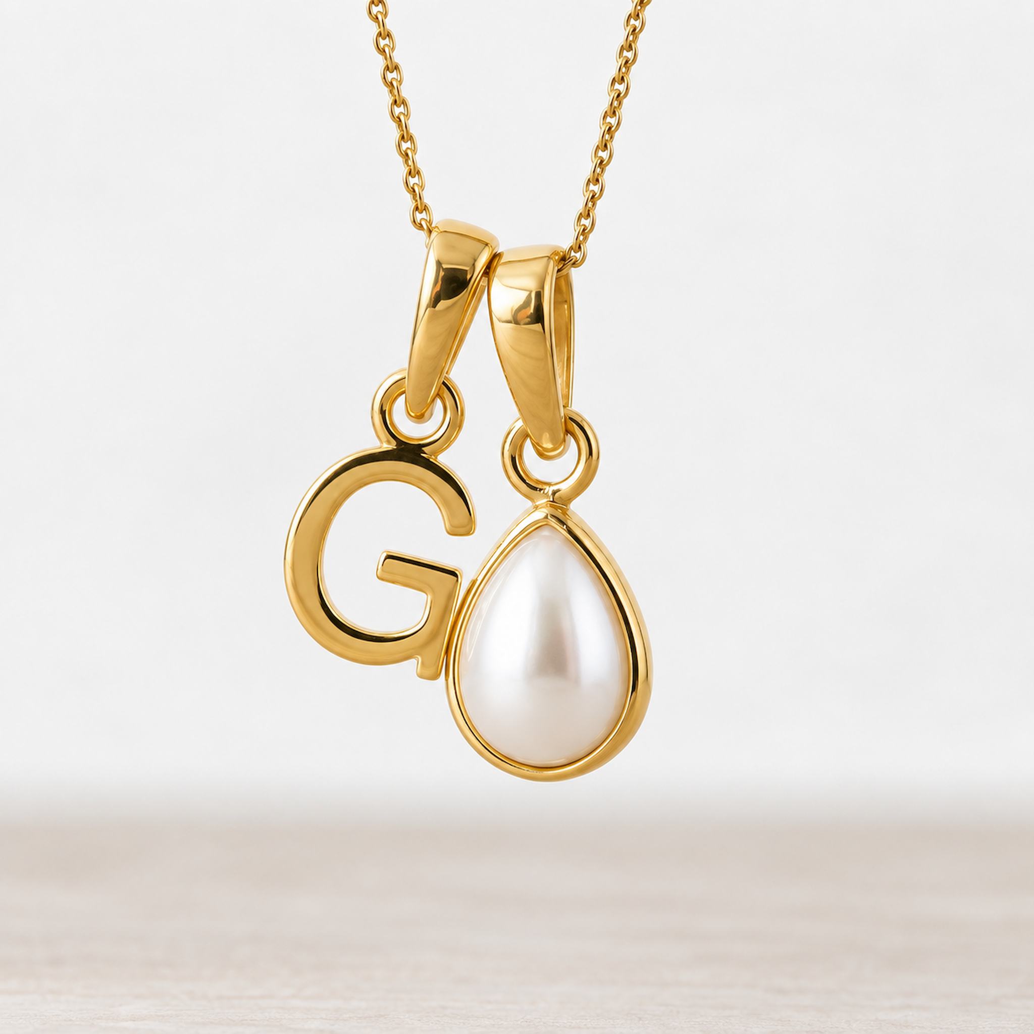 Gold June birthstone necklace with a pear-shaped natural mother of pearl pendant and letter 'G' charm.