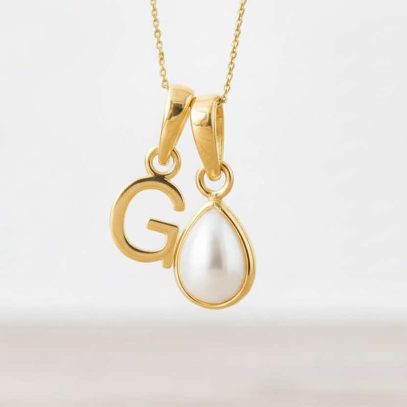 Gold pendant with a letter 'G' and a teardrop-shaped pearl on a light background