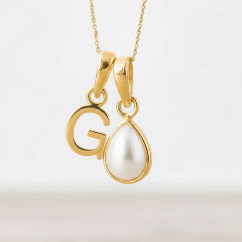 Gold pendant with a letter 'G' and a teardrop-shaped pearl on a light background
