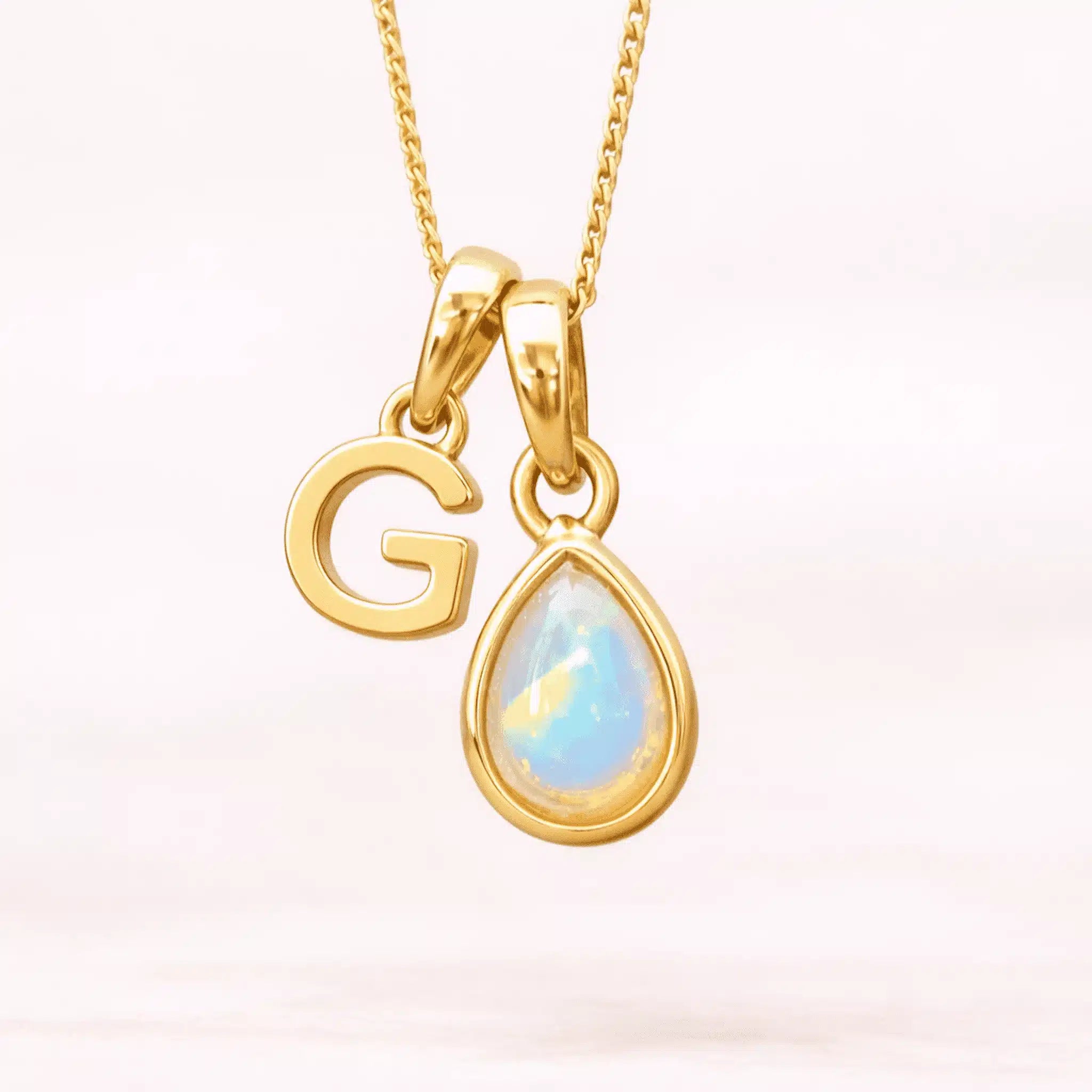Gold October birthstone necklace with a pear-shaped natural opal pendant and letter 'G' charm with a light background.