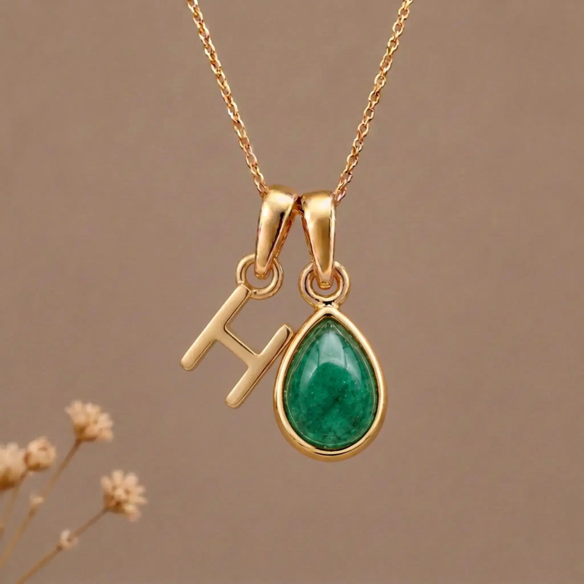 Gold Initial H and May Birthstone Emerald Necklace against a warm background