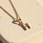 Gold necklace with a 'H' pendant on a beige surface
