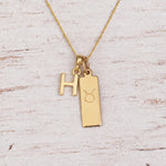 Gold H Initial and Taurus Necklace on a fine gold chain against a light wooden background