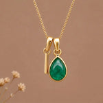 Gold Initial I and May Birthstone Emerald Necklace against a warm background