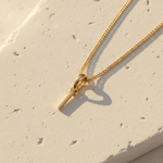 Gold necklace with a small I initial pendant on a light beige surface