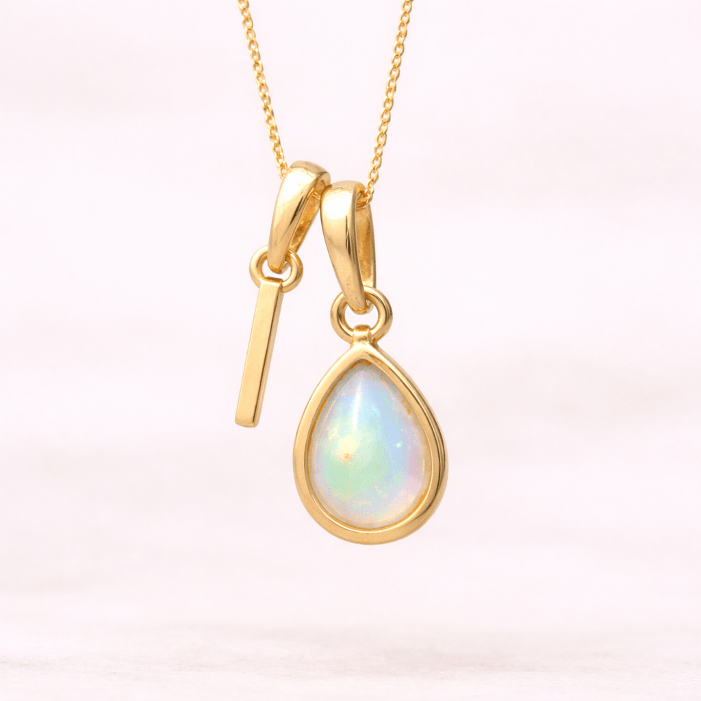 Gold necklace with an 'I' initial charm with a teardrop-shaped opal stone on a white background