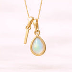 Gold October birthstone necklace with a pear-shaped natural opal pendant and letter 'I' charm with a light background.