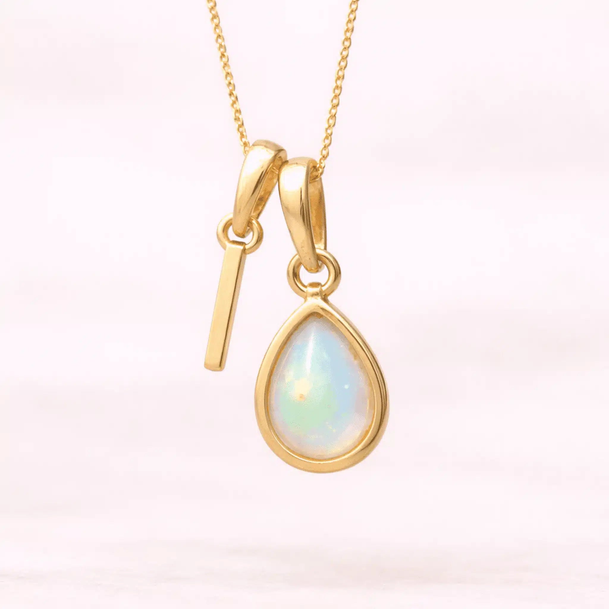 Gold October birthstone necklace with a pear-shaped natural opal pendant and letter 'I' charm with a light background.