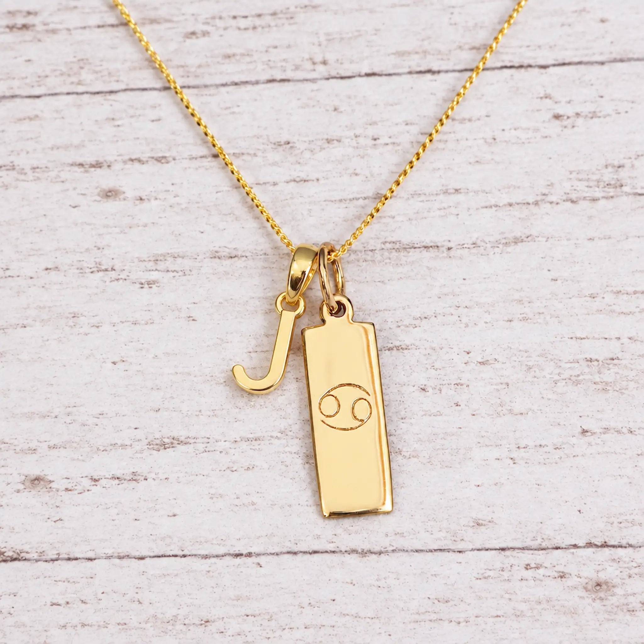 Gold Initial and Cancer Zodiac Necklace with letter J pendant on light wood