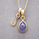 Gold J initial pendant with a purple tanzanite gemstone on a textured gray background