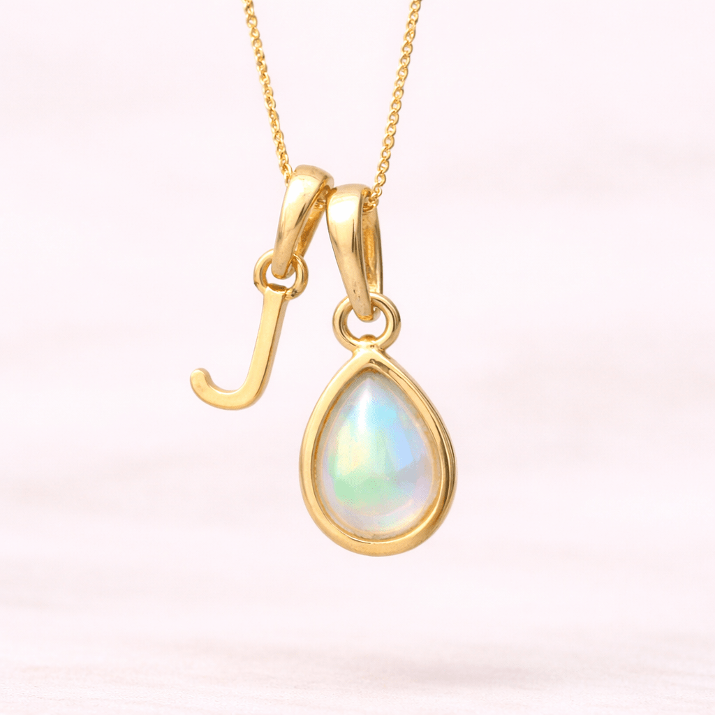 Gold necklace with a 'J' initial pendant with a teardrop-shaped opal gemstone on a white background