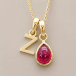 Gold necklace with 'Z' pendant and red natural ruby teardrop-shaped gemstone on a beige background