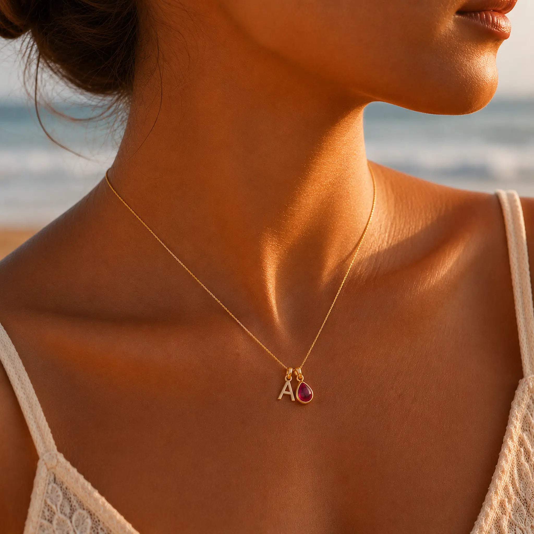 Person wearing a personalised 9k gold-plated initial A and natural pear-shaped July ruby dual-pendant necklace on a fine gold chain.